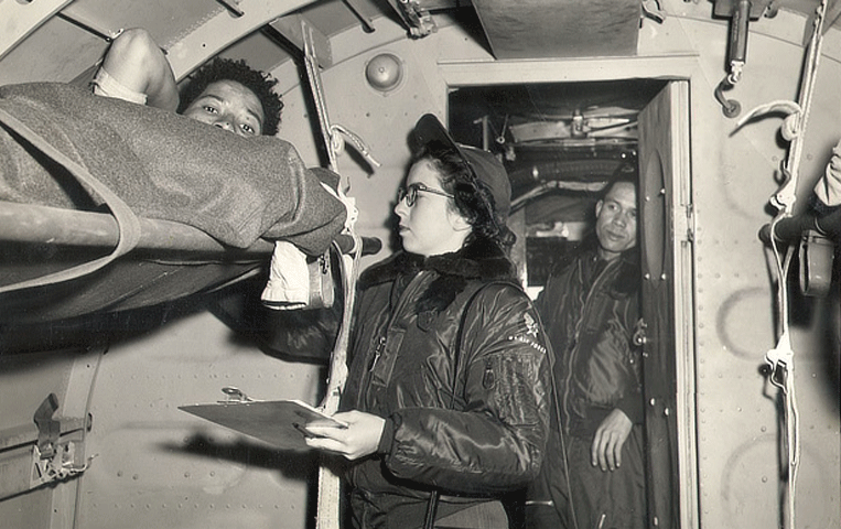 Mary Weiss Hester holding a clipboard caring for a patient onboard a plane.